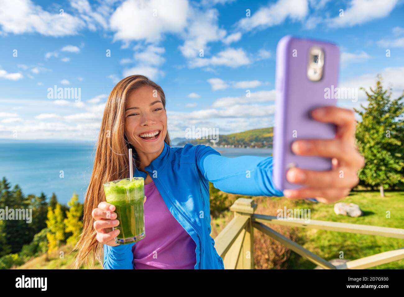 Selfie phone Asian girl social media influencer promoting health benefits of vegan diet green smoothie drink. Healthy detox juice woman drinking Stock Photo