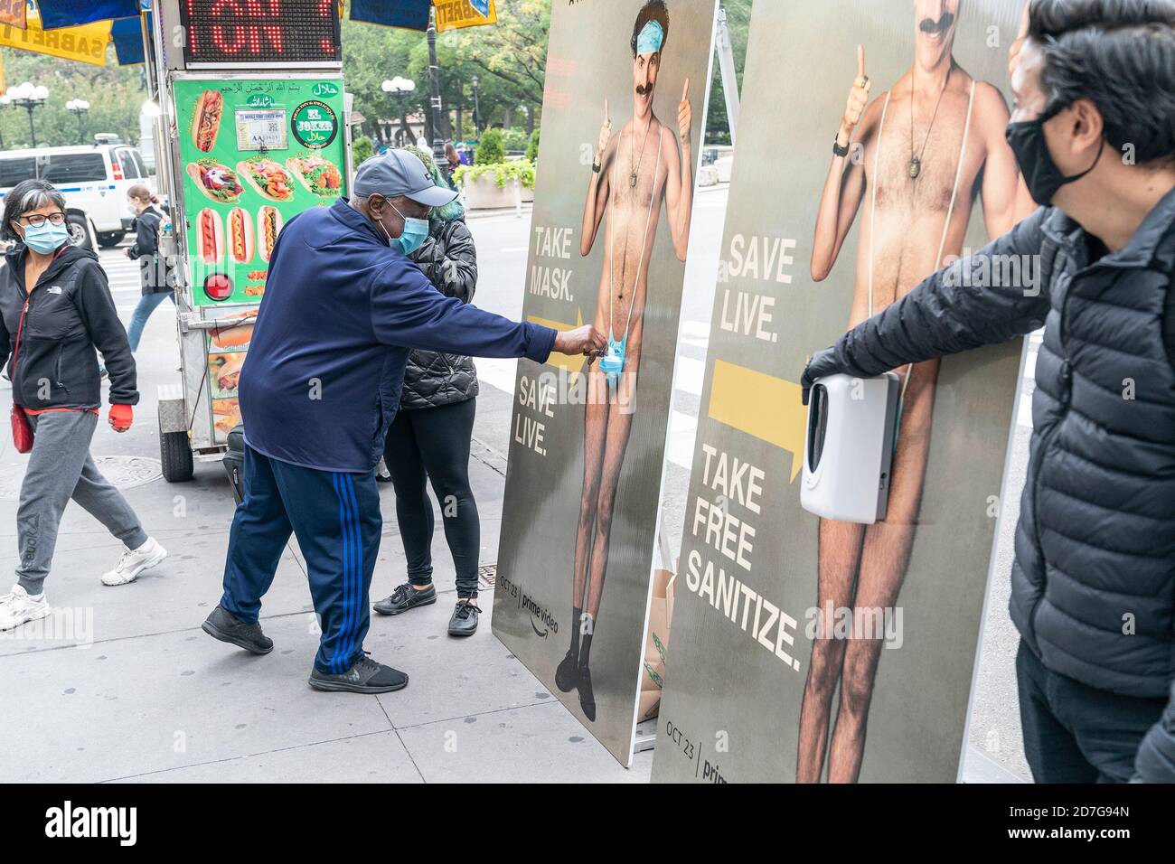 A man picks up facial mask from cutout of Sacha Baron Cohen during promotion of new movie Borat Subsequent Moviefilm produced by Amazon video seen on Union Square. An American mockumentary comedy film written by and starring Sacha Baron Cohen as Kazakhstani television personality Borat Sagdiyev. On cutouts of main character there is reference to the COVID-19 pandemic by replacing Borat's iconic green 'mankini' with a face mask and hand sanitizer for passersby to pick up. (Photo by Lev Radin/Pacific Press) Stock Photo