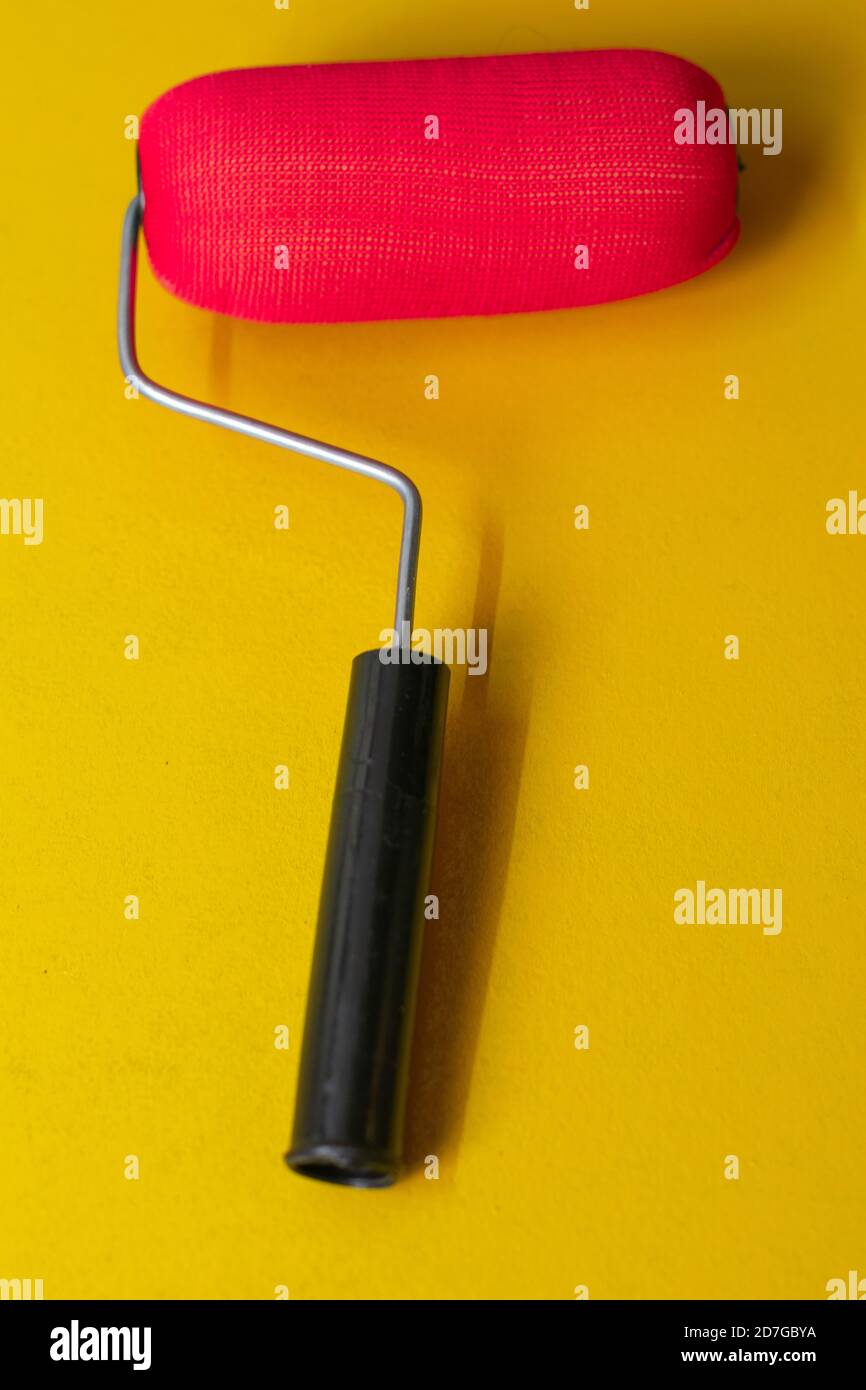 Red paint roller with black handle on yellow background Stock Photo