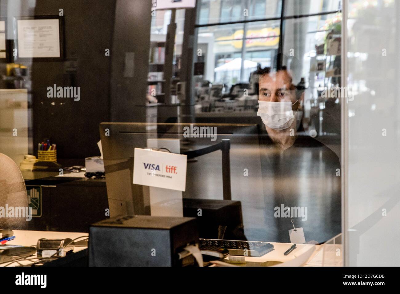A teller wearing a face mask behind his desk at TIFF Bell Lightbox which is nearly-empty during 2020 Toronto International Film Festival, mostly a virtual festival this year. Stock Photo
