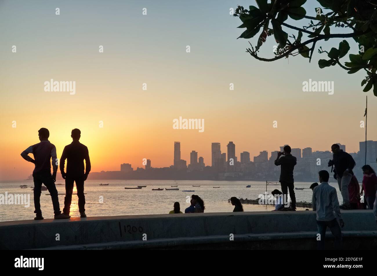 During sunset over the Arabian Sea at Marine Drive, near Chowpatty Beach, Mumbai, local sightseers enjoy the view while standing on the embankment Stock Photo