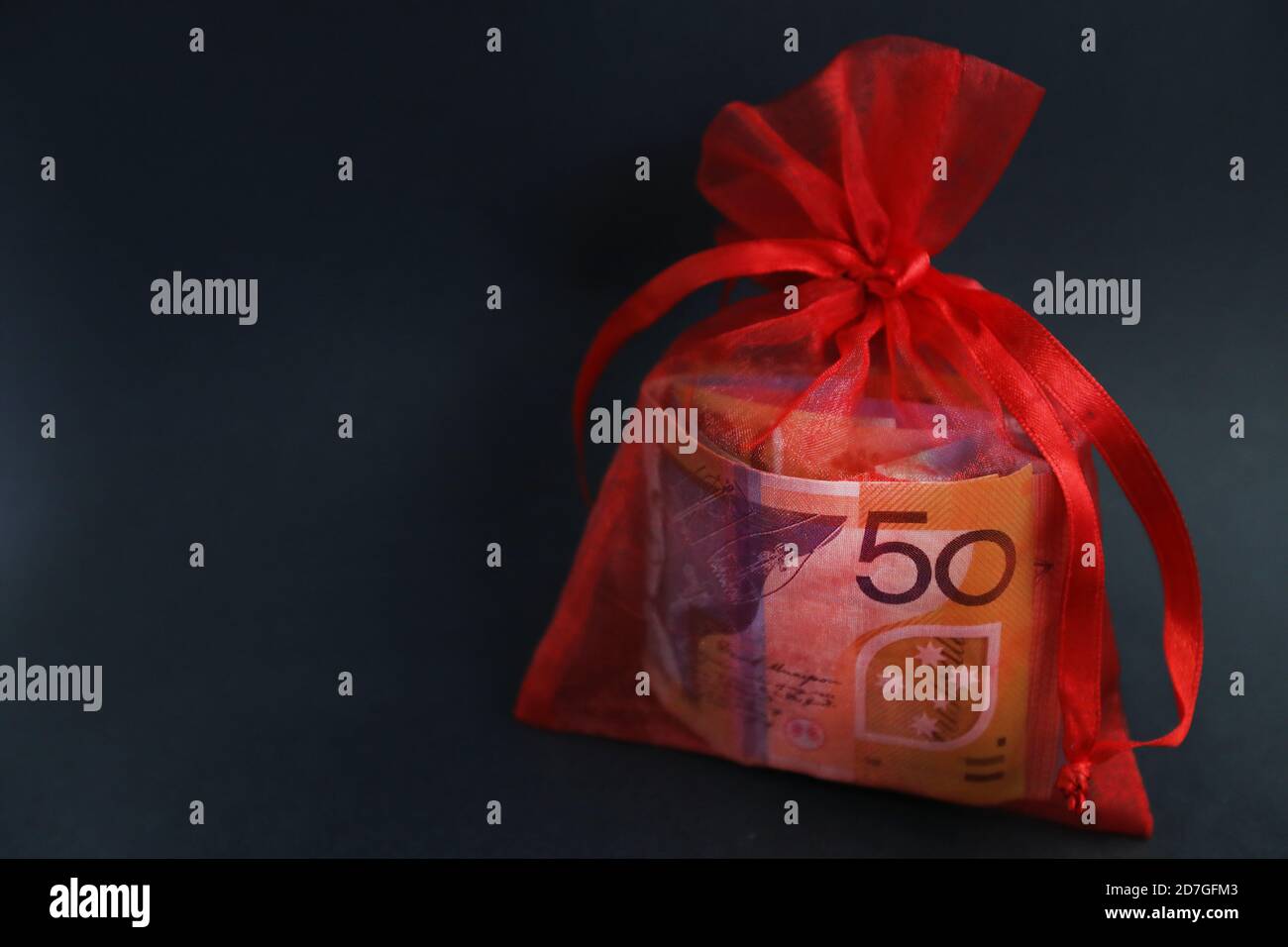 A pretty red glittery bag holding a wad of cash or currency. 50 fifty dollar note clearly visible through bag. Gift, financial assistance, support an Stock Photo