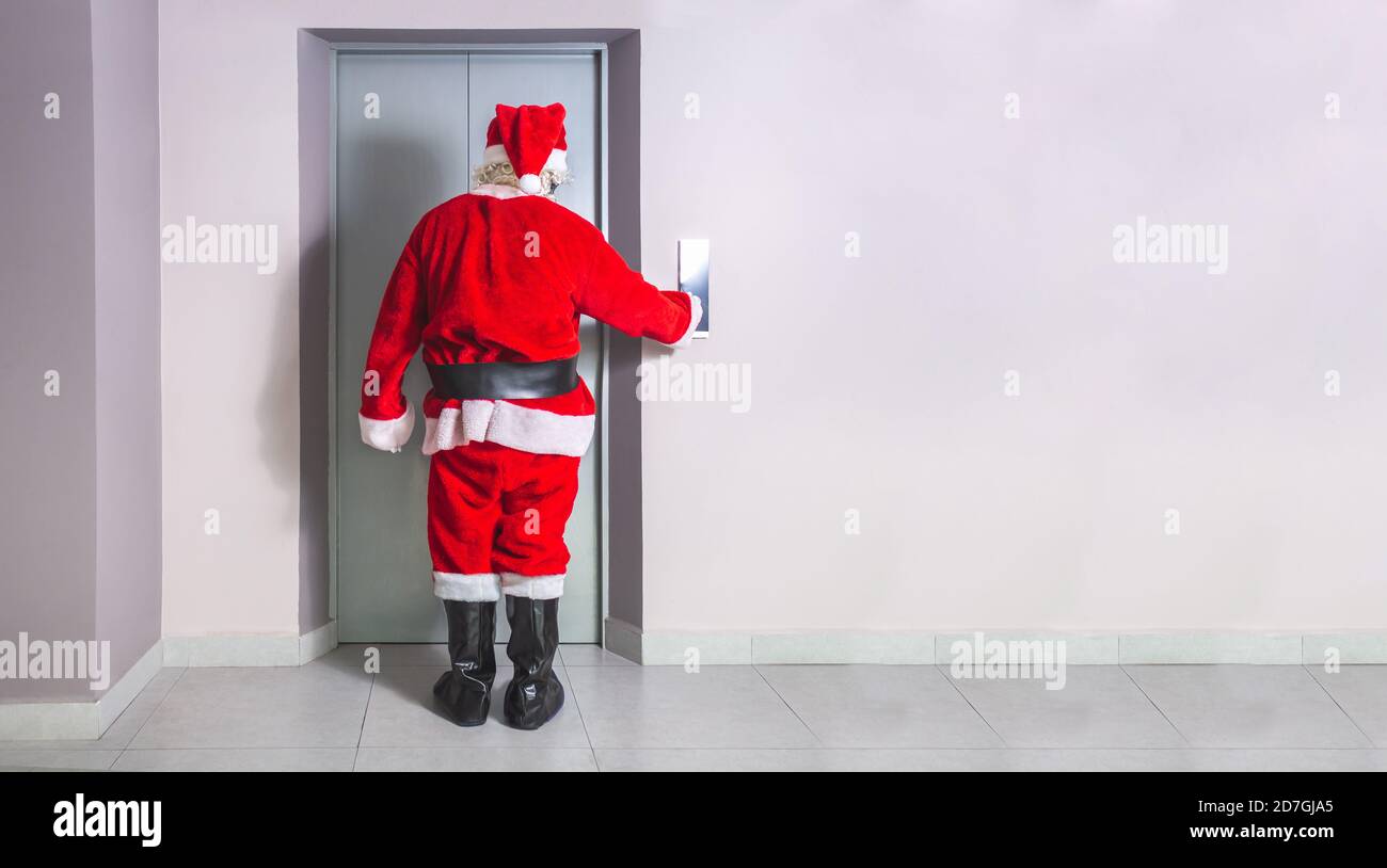 Man disguised as Santa Claus calls the elevator in a building at Christmas in the corridor of a building with a wall with space for text Stock Photo