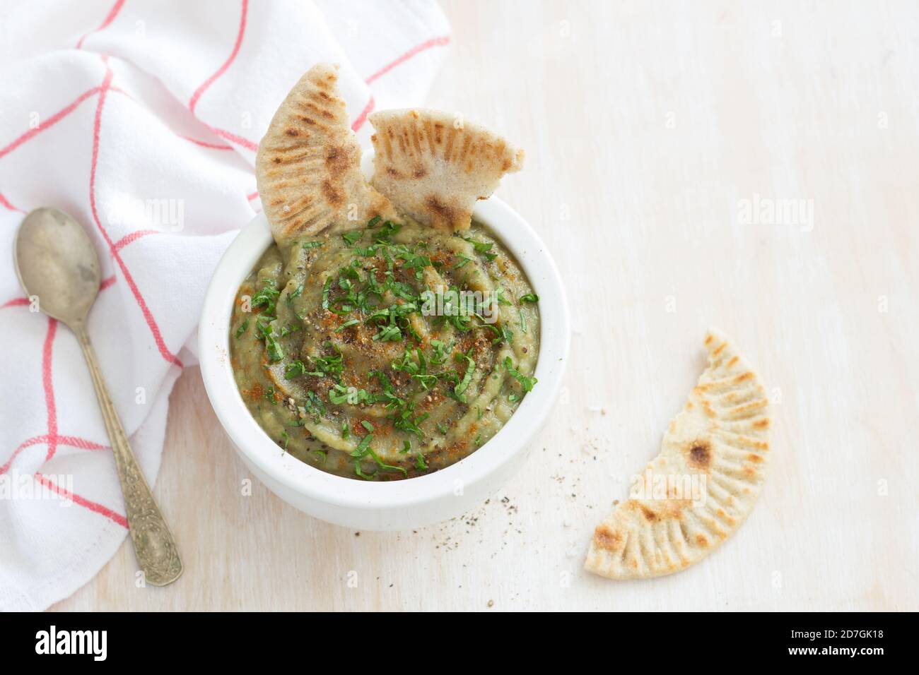 Eggplant dip in a white ceramic bowl with parsley and whole grain flat bread on a light wooden background Stock Photo