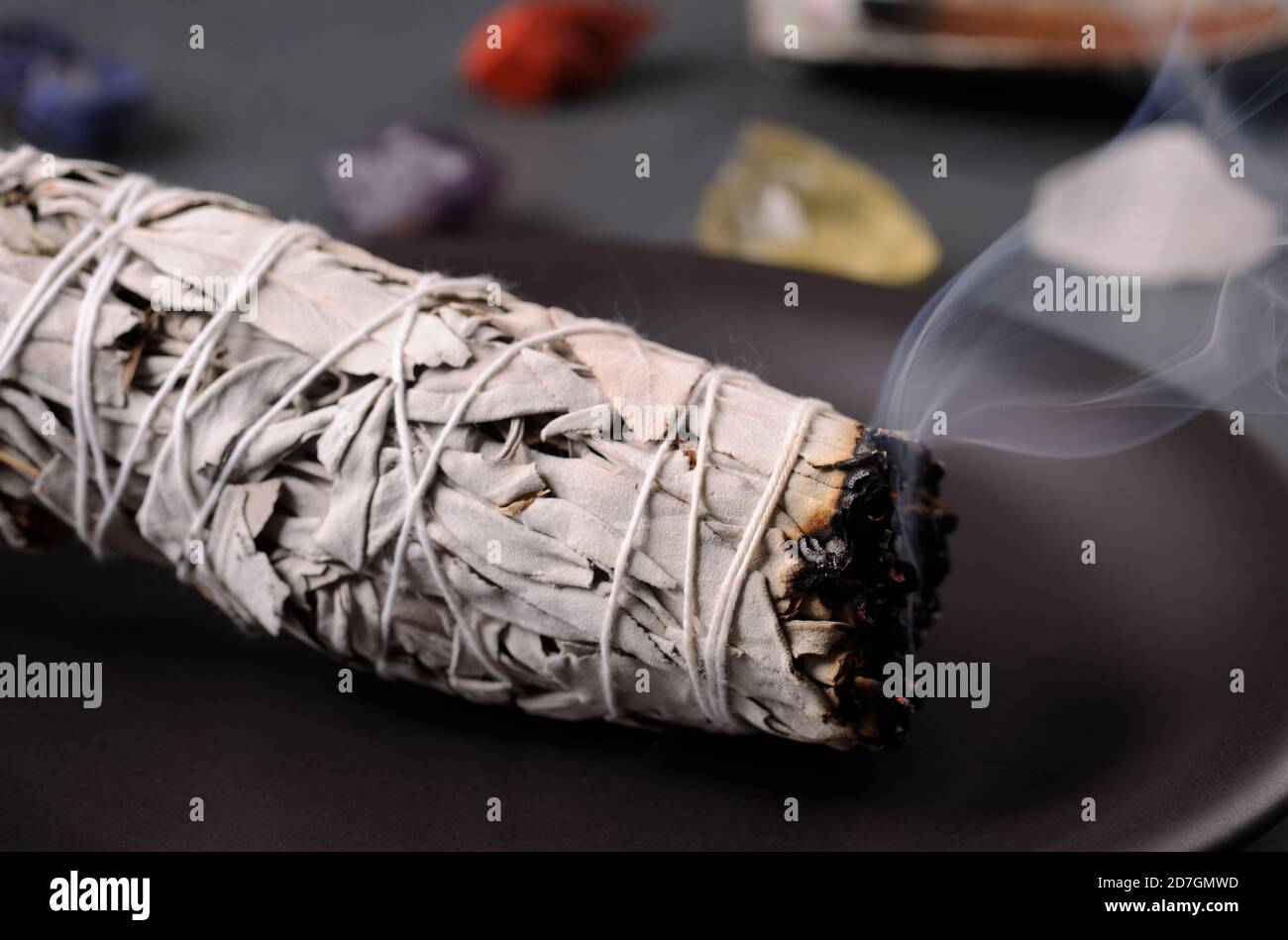 Smudging ritual using burning  leafy bundle of white sage. Image with healing chakra mineral stones. Cleanse the house with aroma smoke. Selective foc Stock Photo