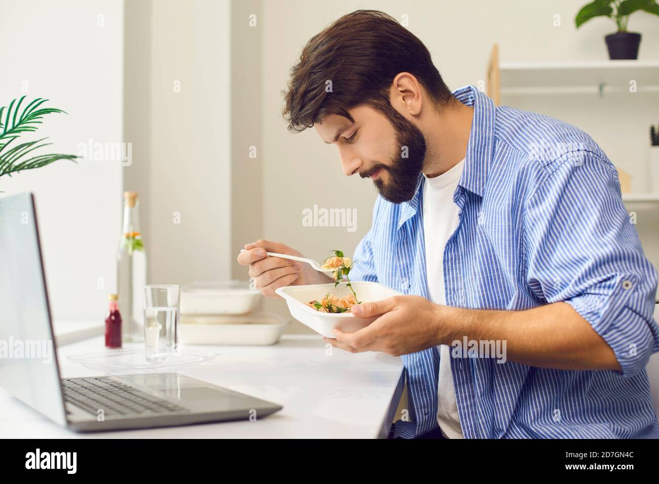 Young employee eating takeaway food during lunch break at home or in the office Stock Photo