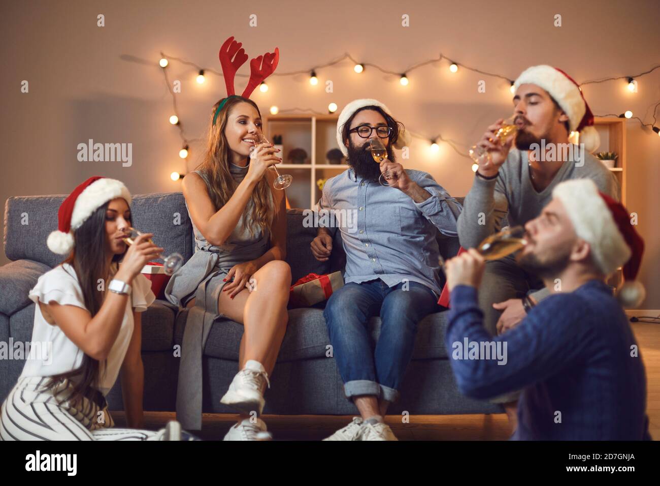 Group of young friends drinking champagne sitting on sofa and floor during Christmas party at home Stock Photo