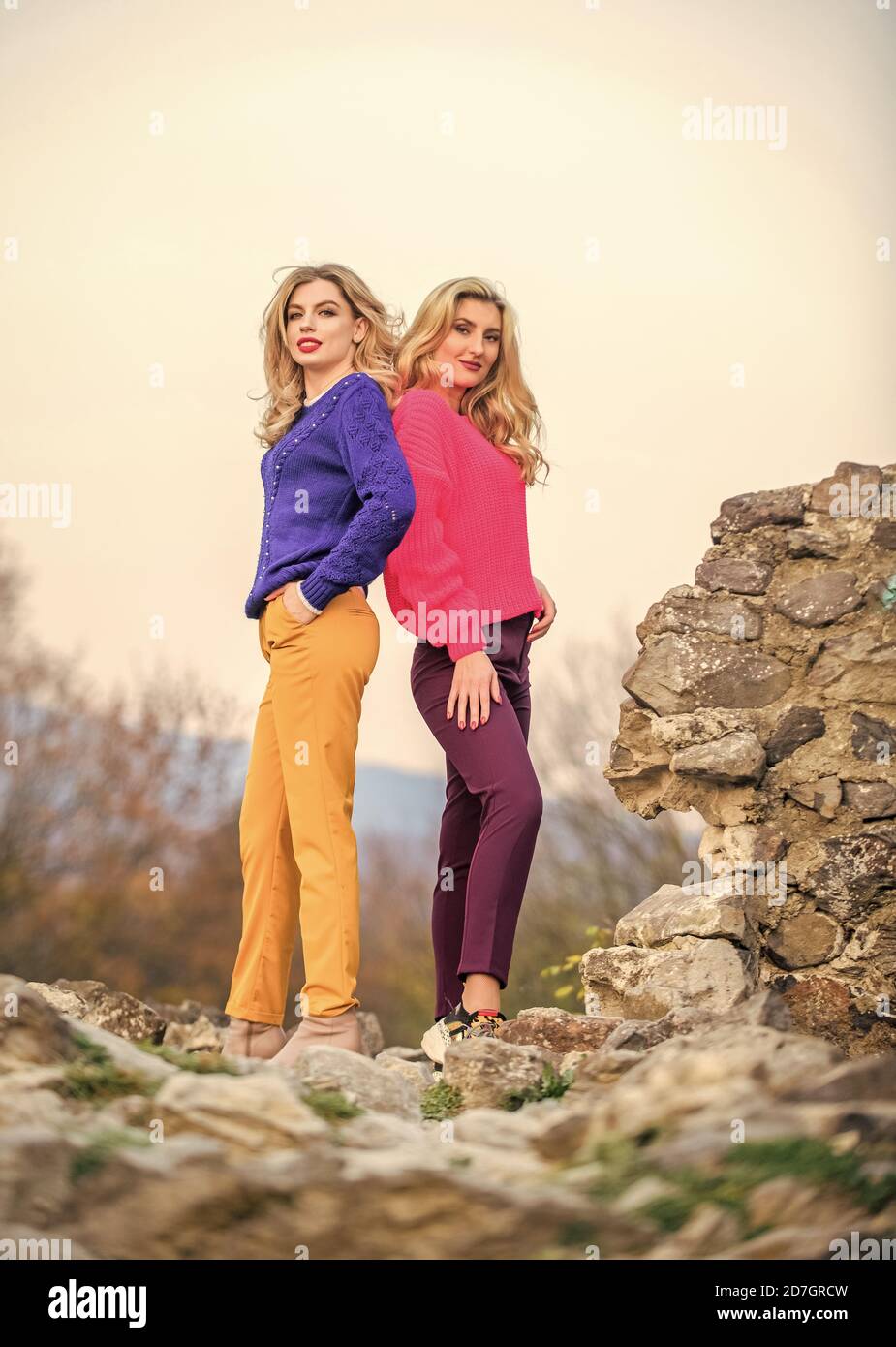 Vivid style concept. Sisters enjoy colorful outfits on gloomy day sky  background. Bright mood. Bright sweaters and pants increase activity add  cheerfulness and improve mood. Girls wear bright clothes Stock Photo 