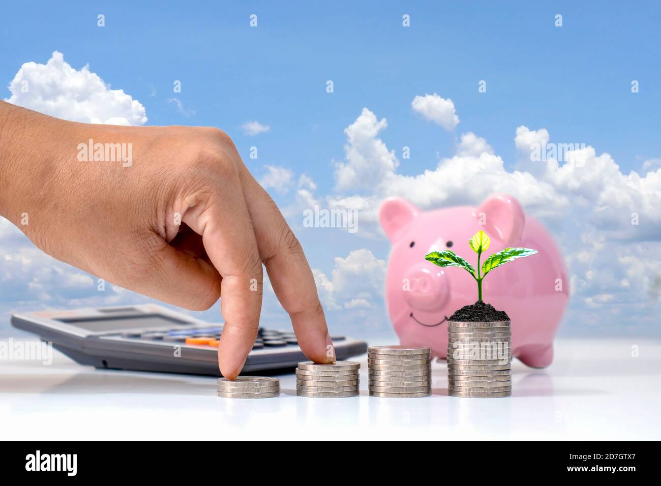 The male investor's hand rests on a pile of flat coins leap and trees on the coin pile of money-saving ideas business growth. Stock Photo