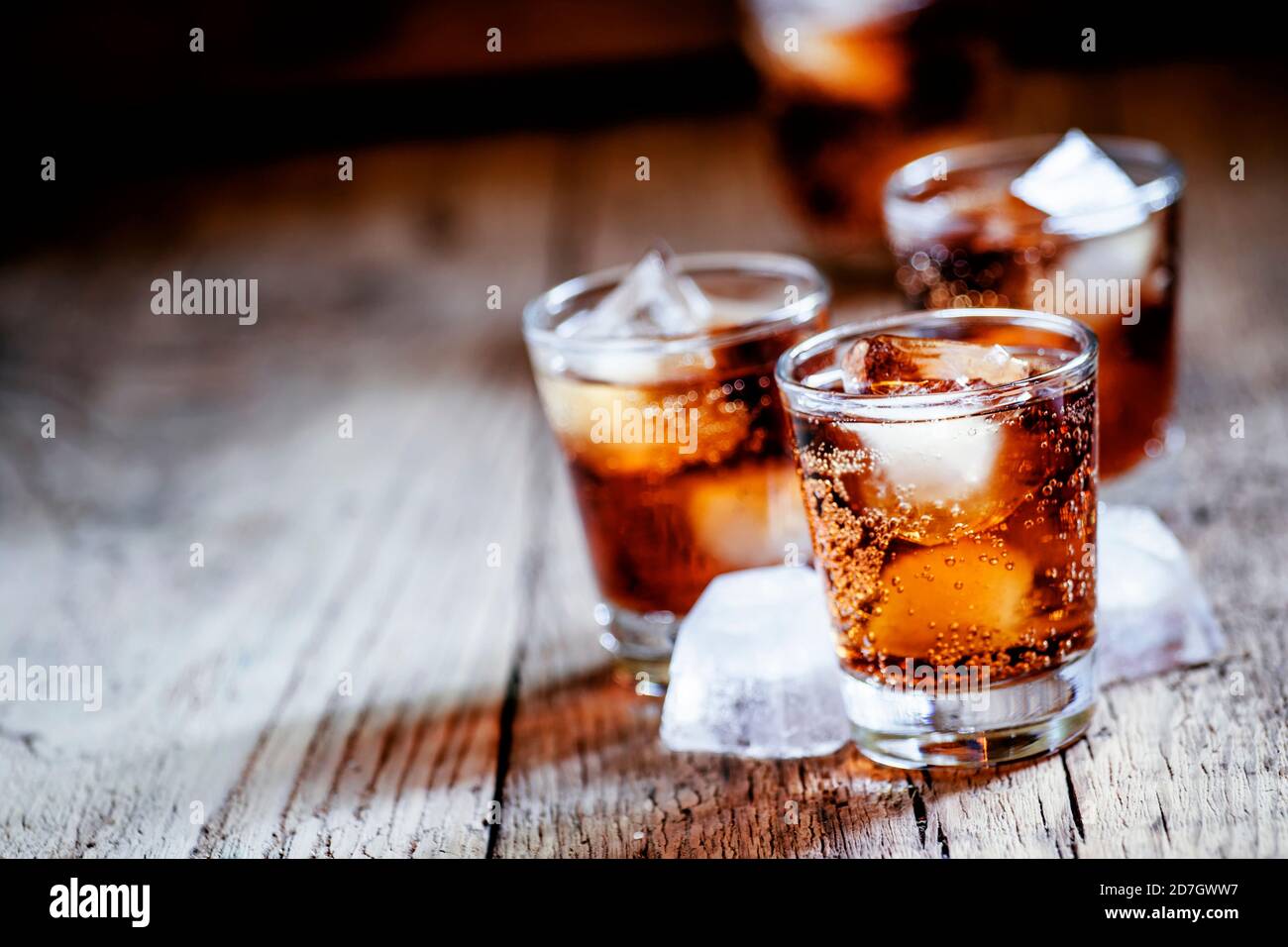 Alcoholic cocktail bourbon cola with whiskey and ice cubes, vintage wooden background, selective focus Stock Photo