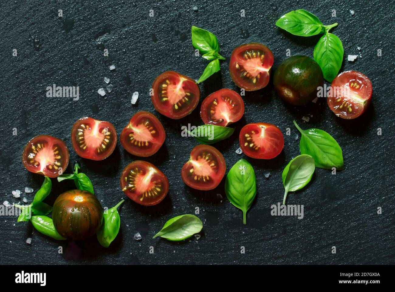 Food background, black and red cherry tomatoes and green basil on a wet ...