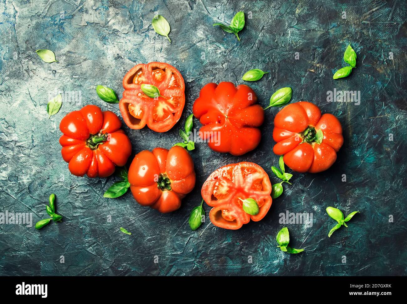 Big red tomatoes with green basil leaves on the old stone table, top ...