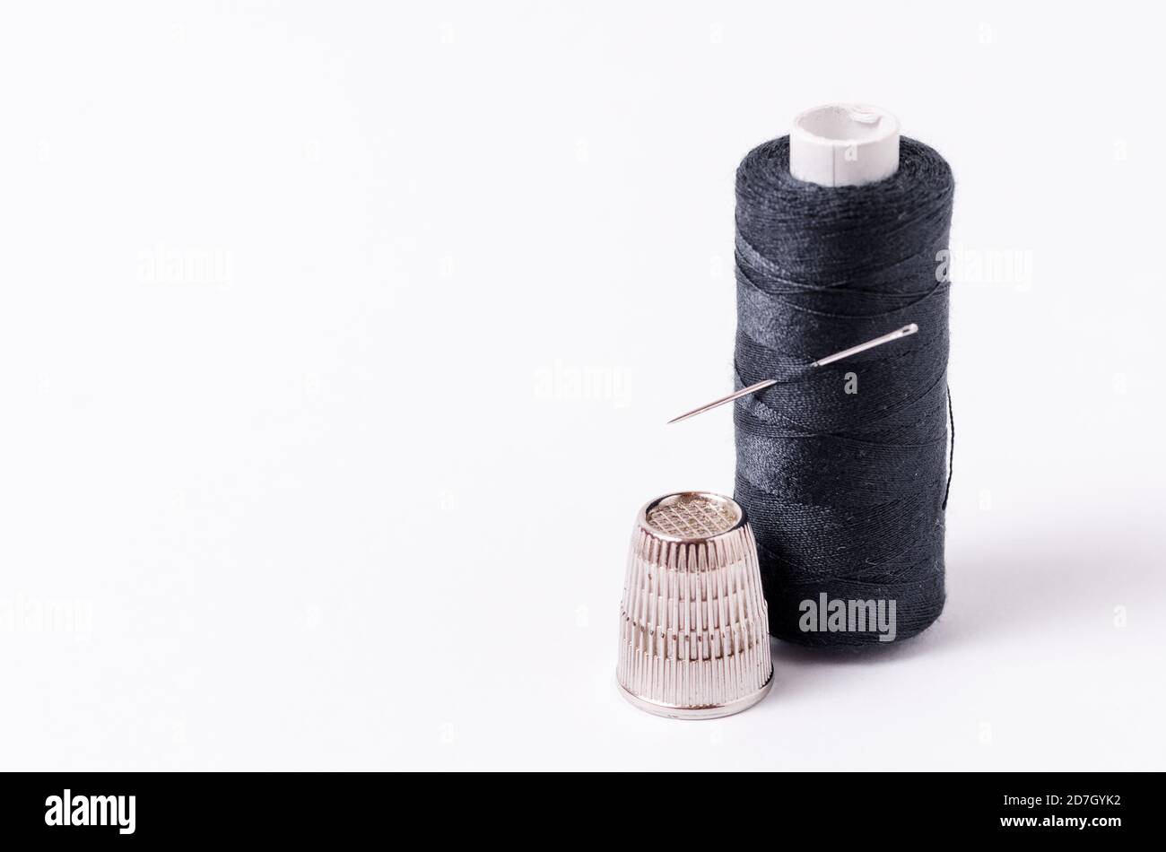 Spool of dark, black thread with needle and one metal thimble on white  background, home crafting, sewing kit, indoors, close-up Stock Photo - Alamy