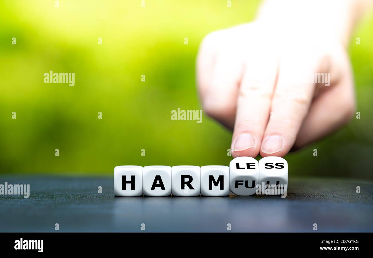 Hand turns dice and changes the word 'harmful' to 'harmless'. Stock Photo