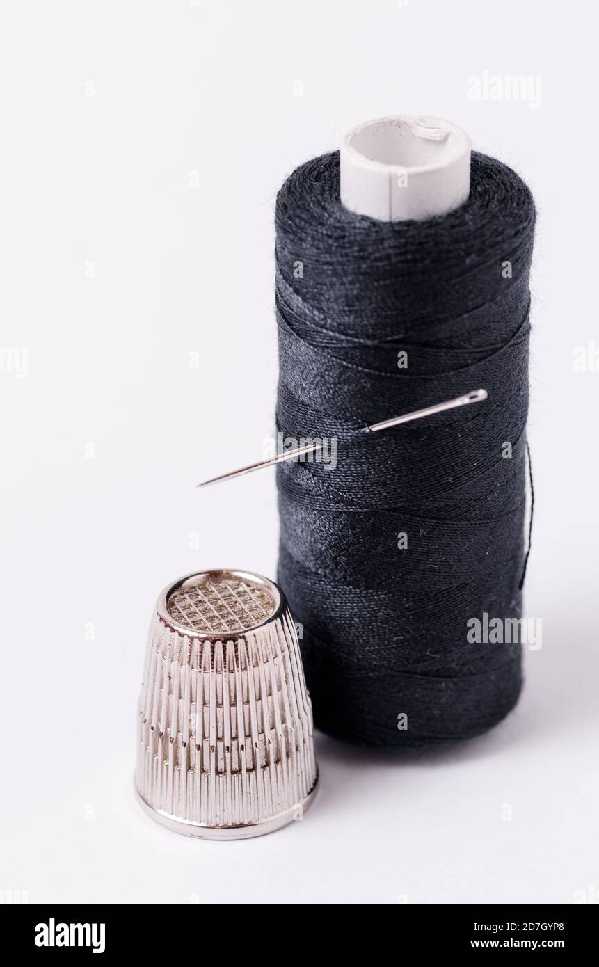 Spool of dark, black thread with needle and one metal thimble on