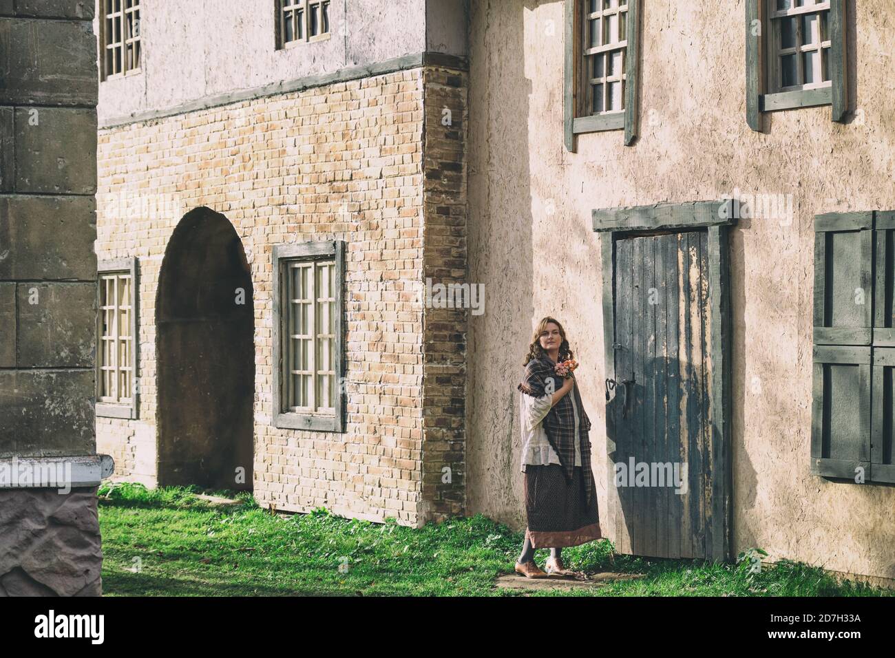 woman with flowers in retro clothes stands at the door of an old ...