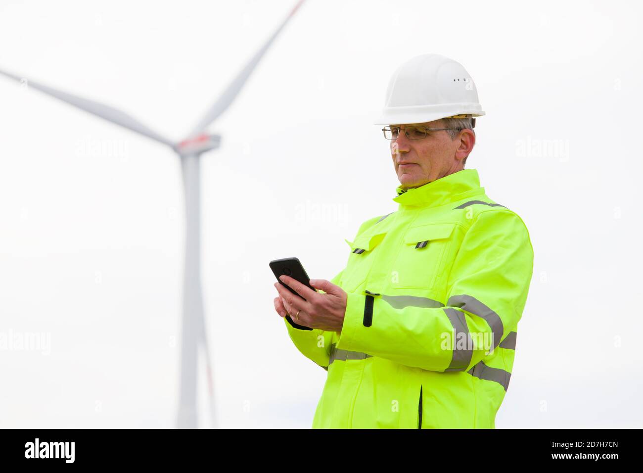 Mature engineer looking at smart phone in front of a wind turbine - focus on  the face Stock Photo