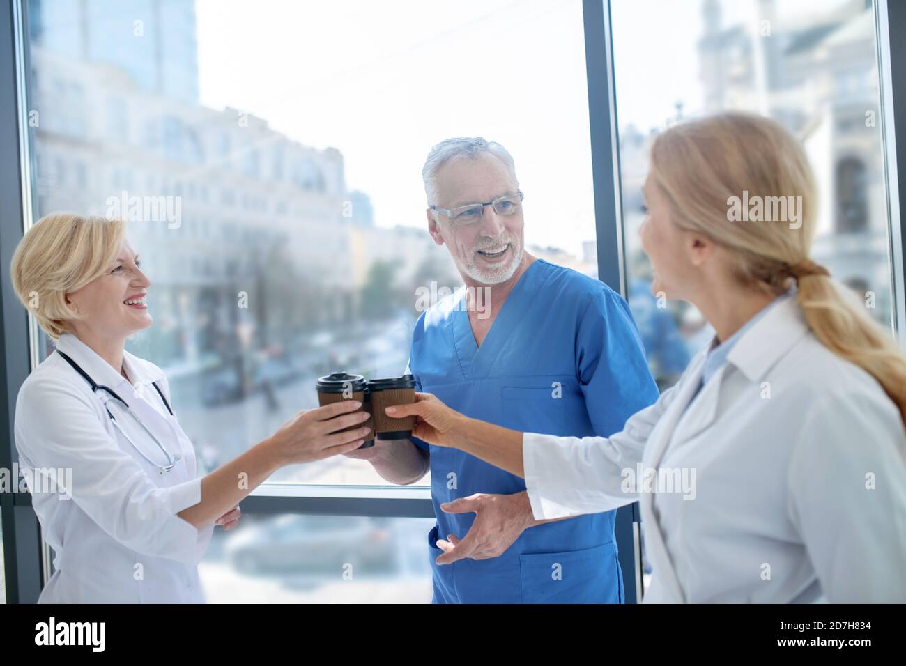 Smiling medical workers drinking coffee, having friendly conversation Stock Photo