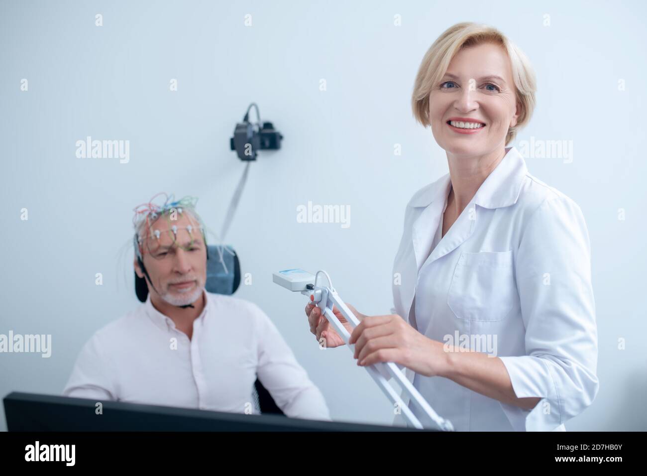 Smiling female neurologist holding lamp, male patient undergoing electroencephalogram Stock Photo