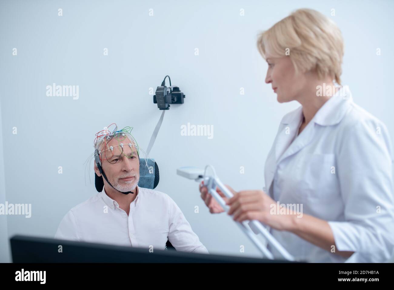 Female neurologist holding lamp, looking at male patient undergoing electroencephalogram Stock Photo