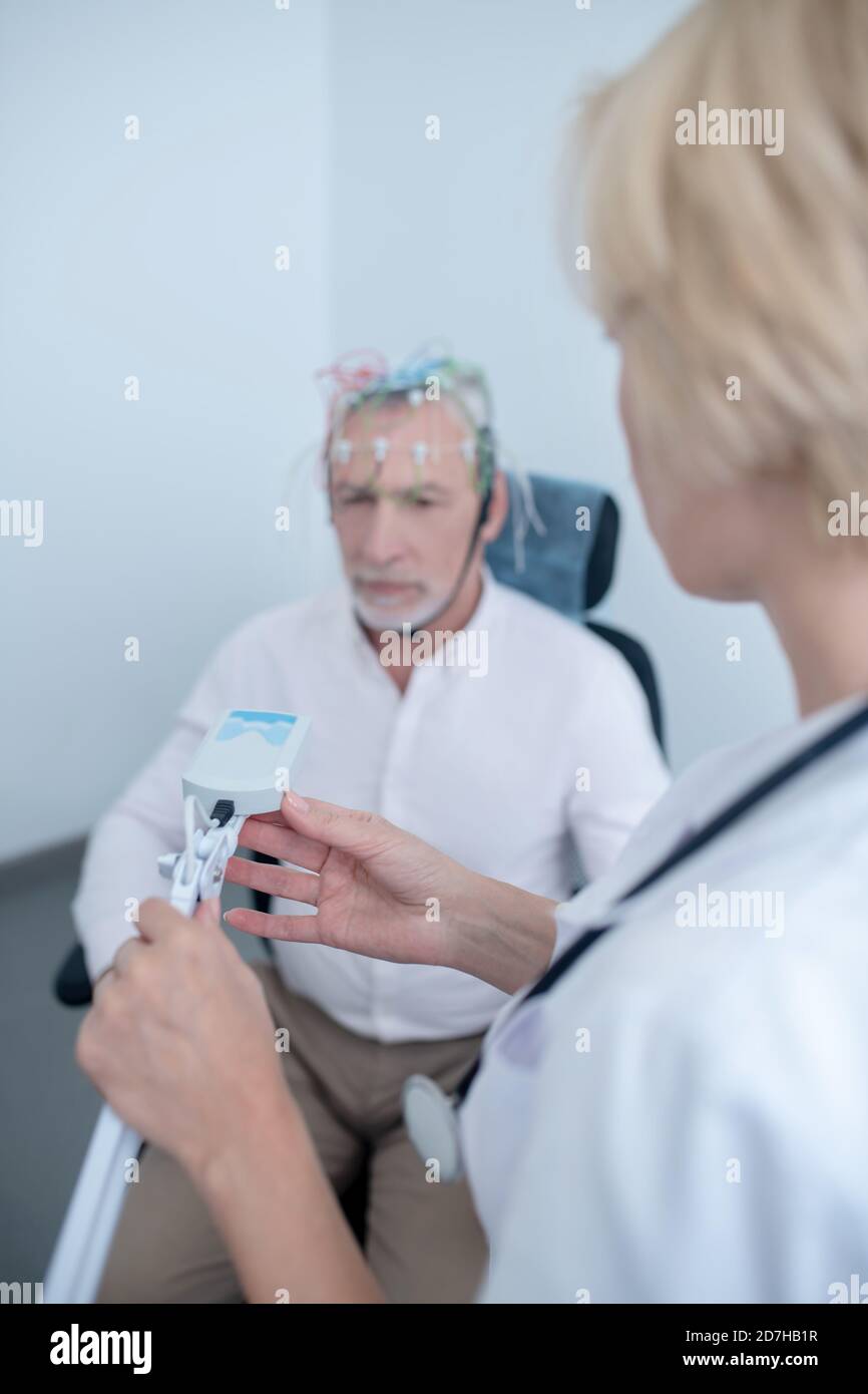 Female neurologist holding lamp near male patient undergoing electroencephalogram Stock Photo