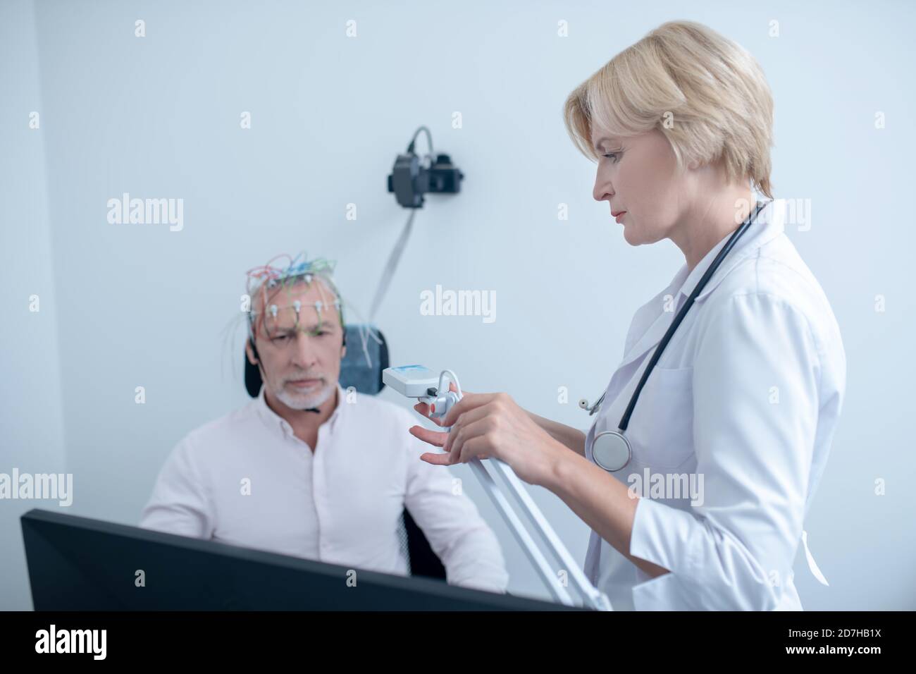 Female neurologist watching gray-haired male patient undergoing electroencephalogram Stock Photo