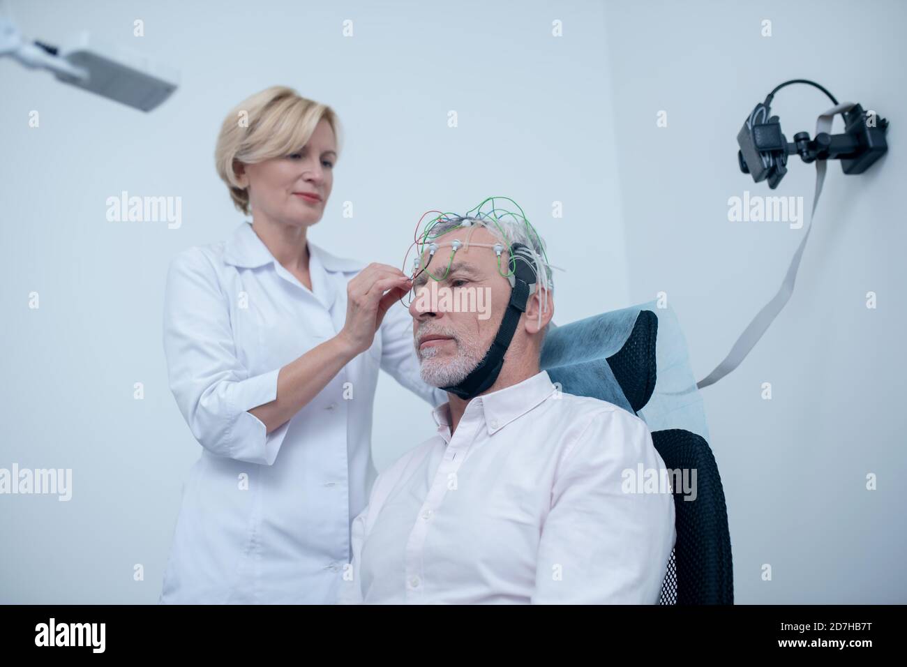 Female neurologist adjusting electrode cap on gray-haired male patient head Stock Photo