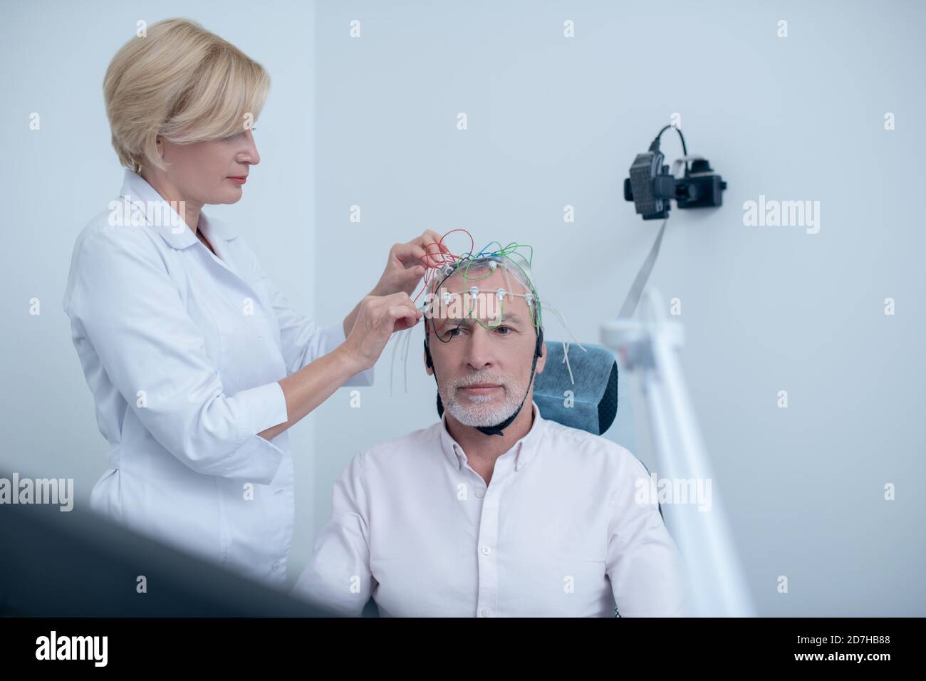Female neurologist adjusting electrodes on gray-haired male patient head Stock Photo