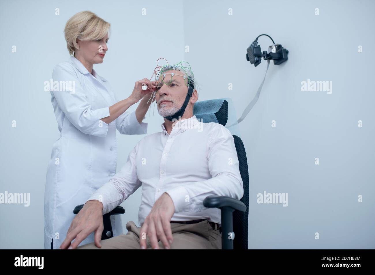 Female neurologist placing electrodes on gray-haired male patient head Stock Photo