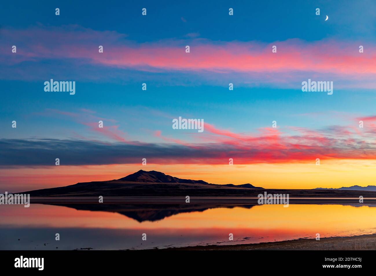 The image of Antelope Island reflects on the water of the Great Salt Lake as the sunset afterglow reflects in the clouds above. Stock Photo