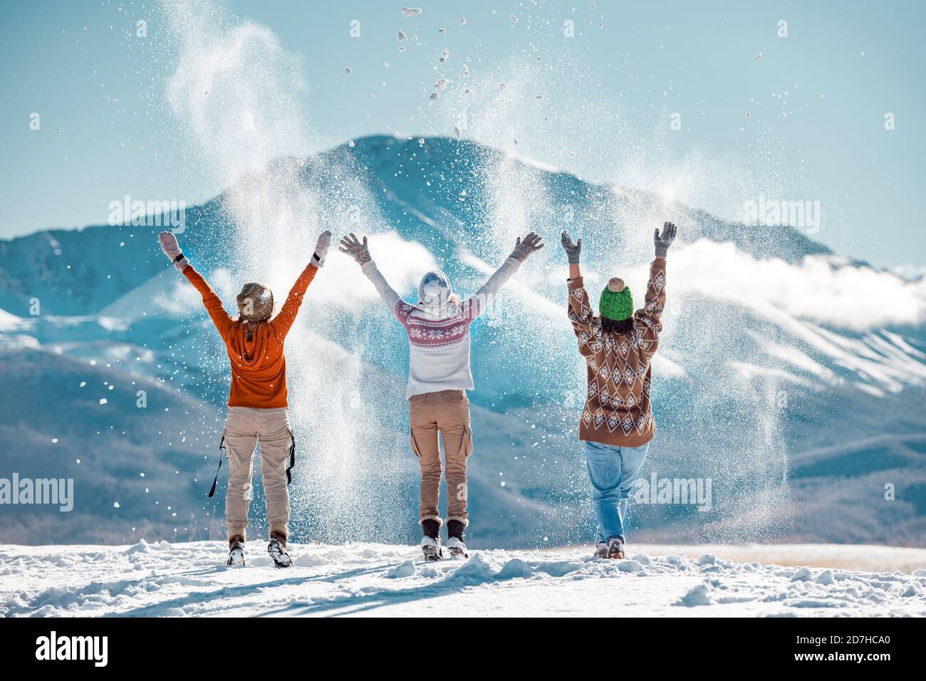Three happy adult girls are having fun and throws first snow on background of mountains. Travel in winter time concept Stock Photo