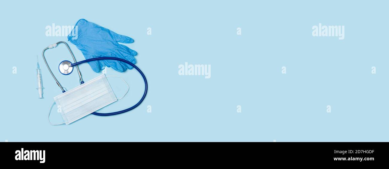 A stethoscope with a medical mask and gloves on a light blue and panoramic background. Copy space Stock Photo