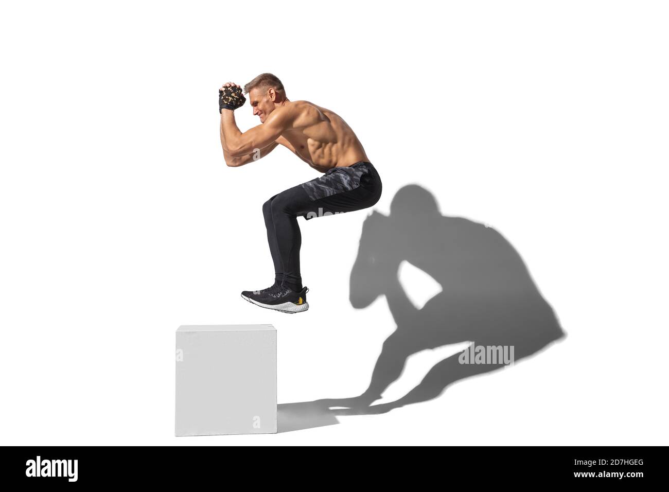 Activity, jumpbox. Stylish young male athlete on white studio background, portrait with shadows. Sportive fit model in motion and action. Body building, healthy lifestyle, style concept. Stock Photo