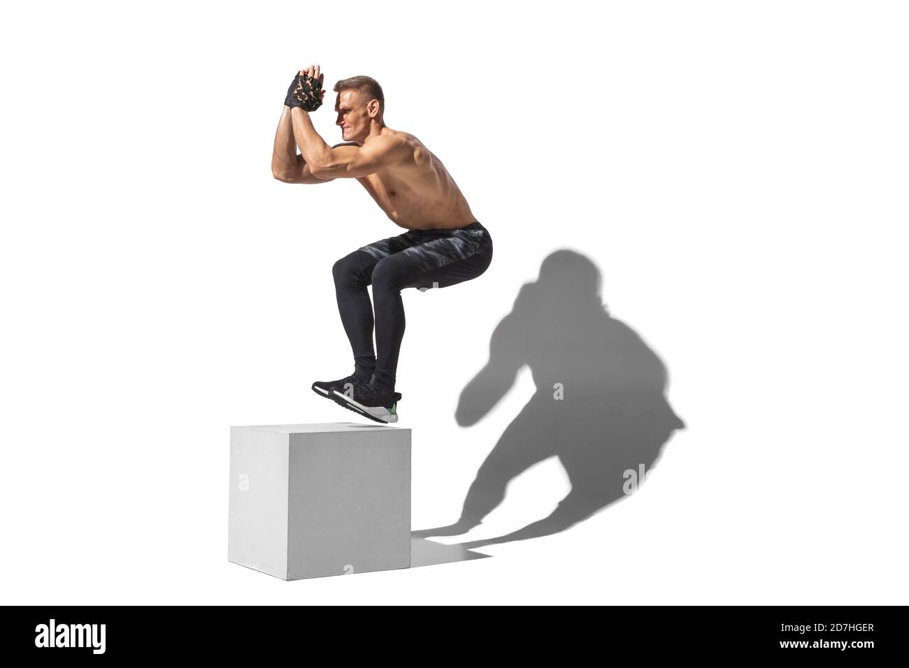 Activity, jumpbox. Stylish young male athlete on white studio background, portrait with shadows. Sportive fit model in motion and action. Body building, healthy lifestyle, style concept. Stock Photo