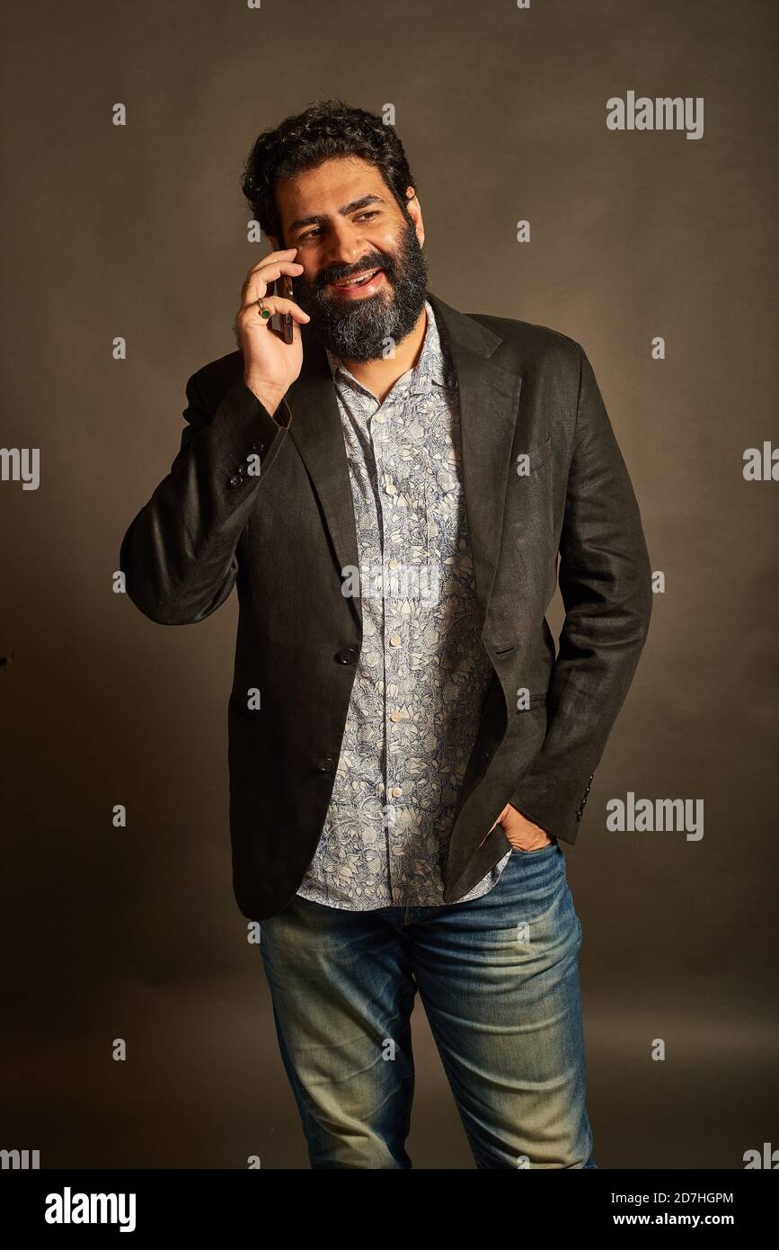 Young Indian man, in a blazer and denims, talking on his phone Stock Photo