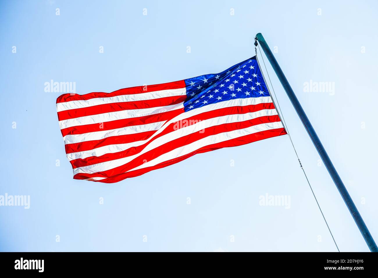 Front view of the American flag on a flagpole fluttering in wind on sky ...