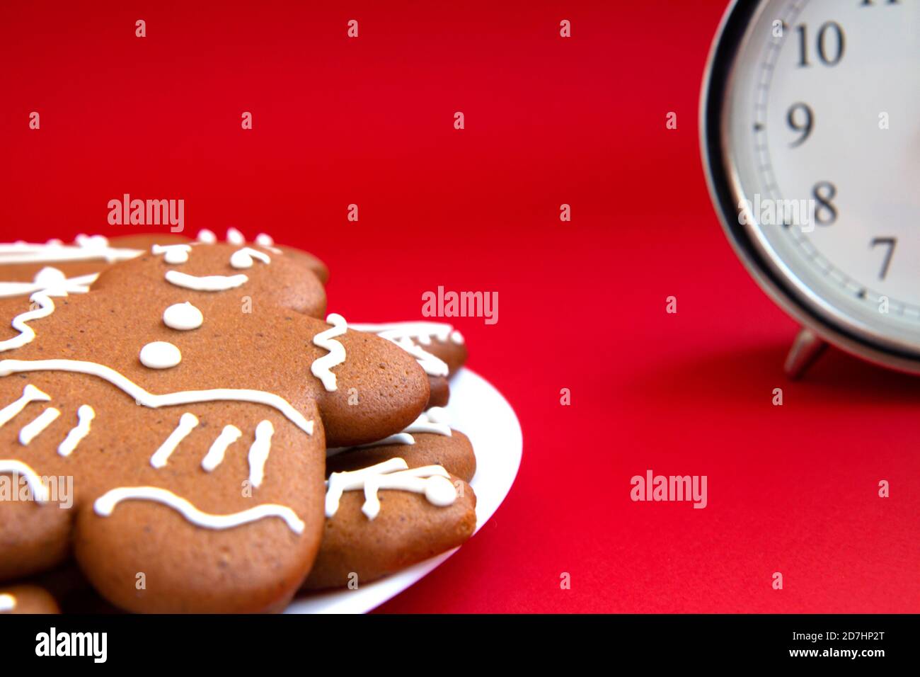 Beautiful vintage silver alarm clock and in the foreground plate of gingerbread cookies on a bright red background. Time concept. Holiday routine. Wai Stock Photo