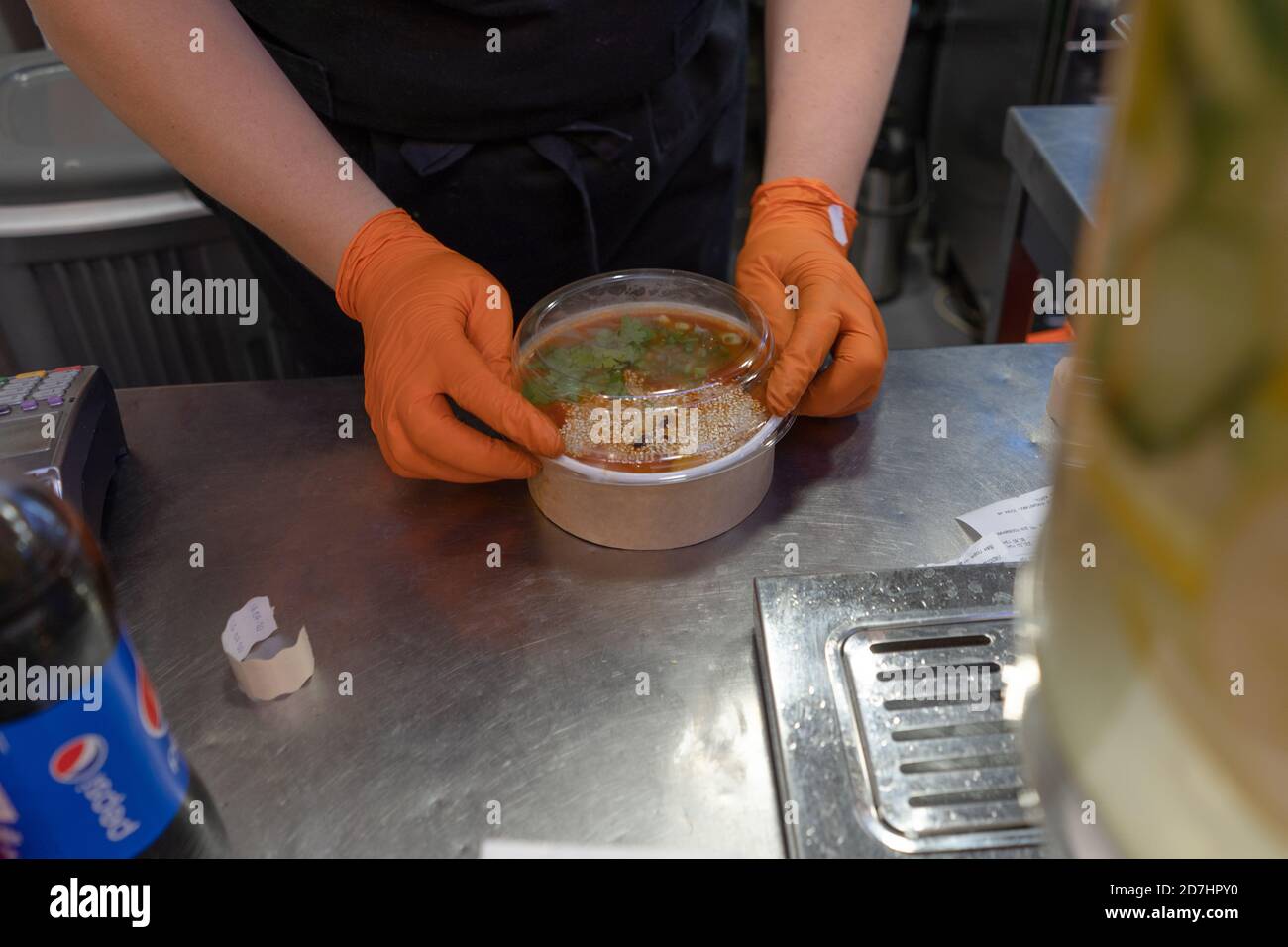 Worker wearing gloves packs tom yum soup into container. Asian restaurant. June 2020. Kyiv, Ukraine Stock Photo