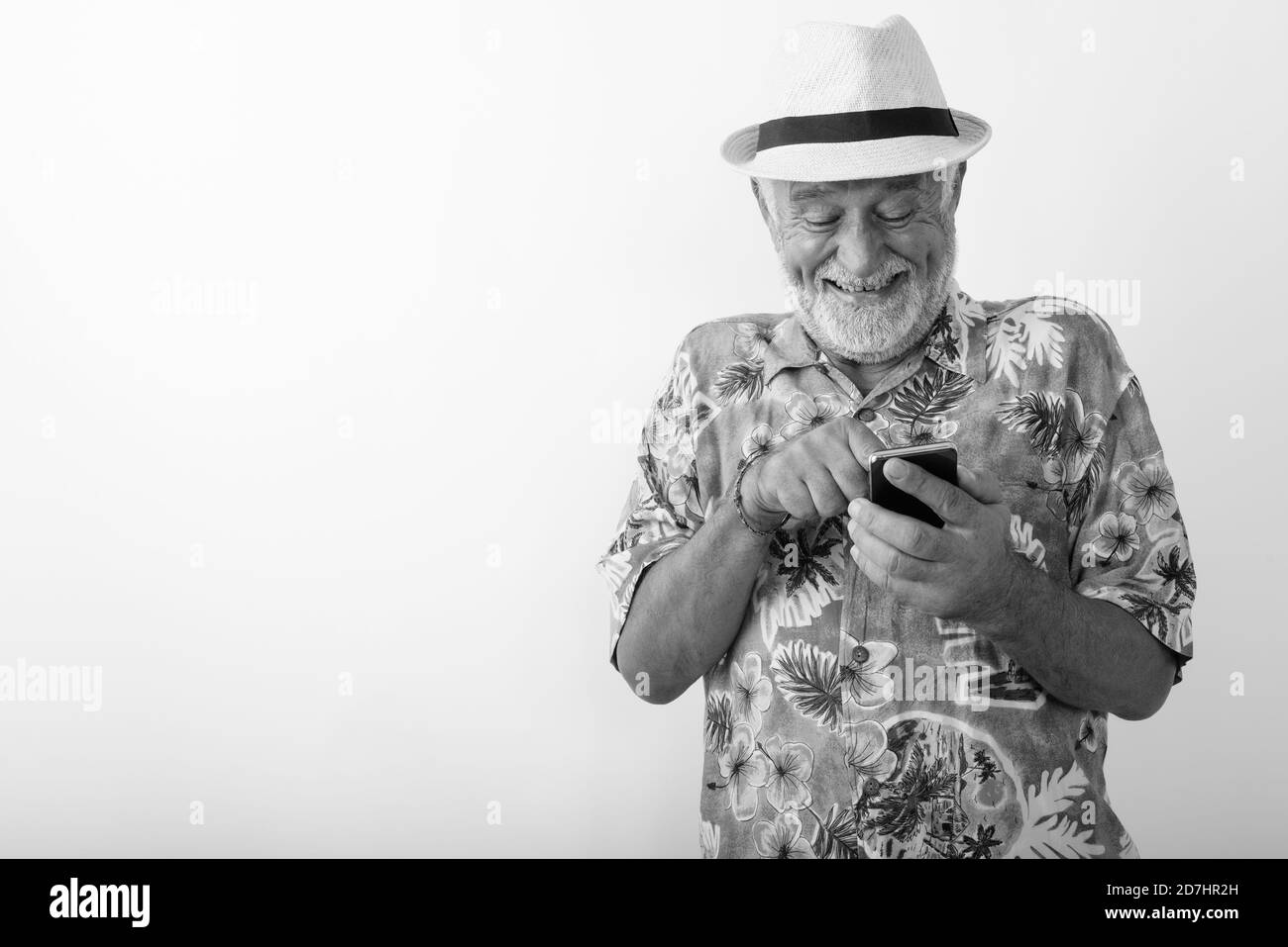 Studio shot of happy senior bearded tourist man smiling and giggling while using mobile phone against white background Stock Photo