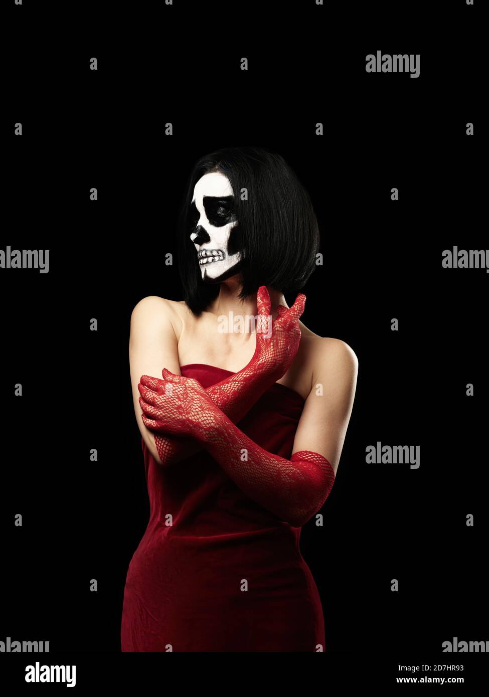 woman of Caucasian appearance dressed in a red velvet dress, long fishnet gloves. Halloween Skeleton Makeup, Black Background Stock Photo