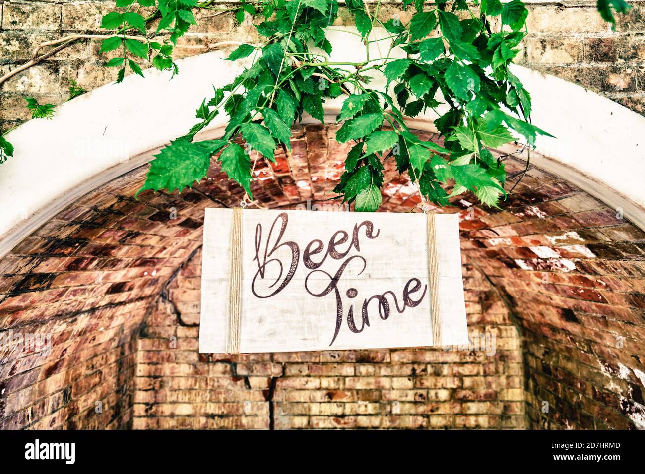View of handwritten board with beer time text hanging under arch and ...