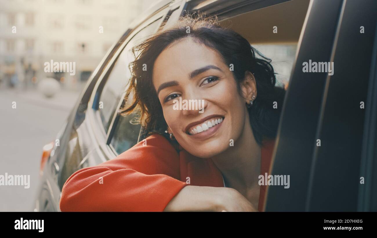 Happy Beautiful Woman Riding on a Back Seat of a Car, Looks out of the Open Window in Wonder of the Big City. Traveling Girl Experience Magic of the Stock Photo