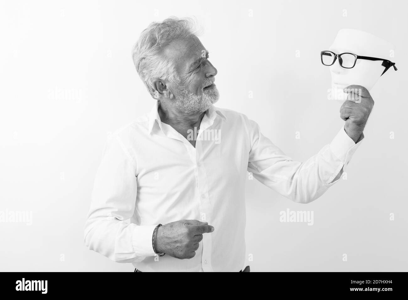 Profile view of happy senior bearded man smiling and looking at white mask with eyeglasses against white background Stock Photo