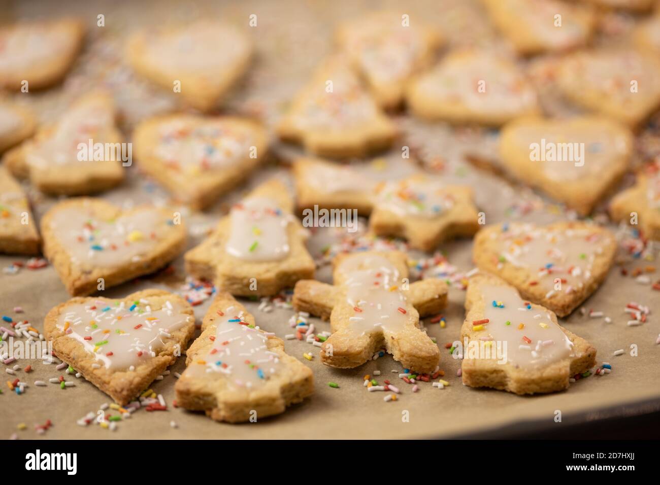 Christmas baking: Shortcrust cookies with sugar icing on baking paper. Shallow depth of field Stock Photo