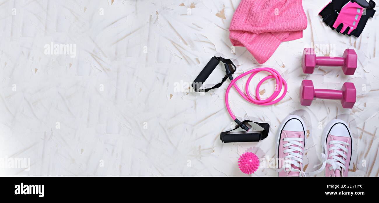 Sports still life in top view with pink tones, sneakers, dumbbells, rubber band, massage ball and towel, panoramic format. Copy space. Healthy concept Stock Photo