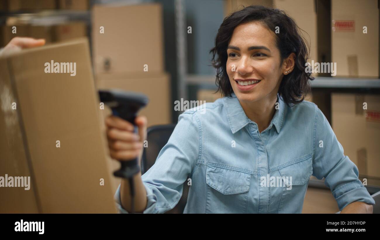 Female Inventory Manager Scans Cardboard Box and with Barcode Scanner, Male Worker Holds Package. In the Background Rows of Cardboard Boxes with Stock Photo