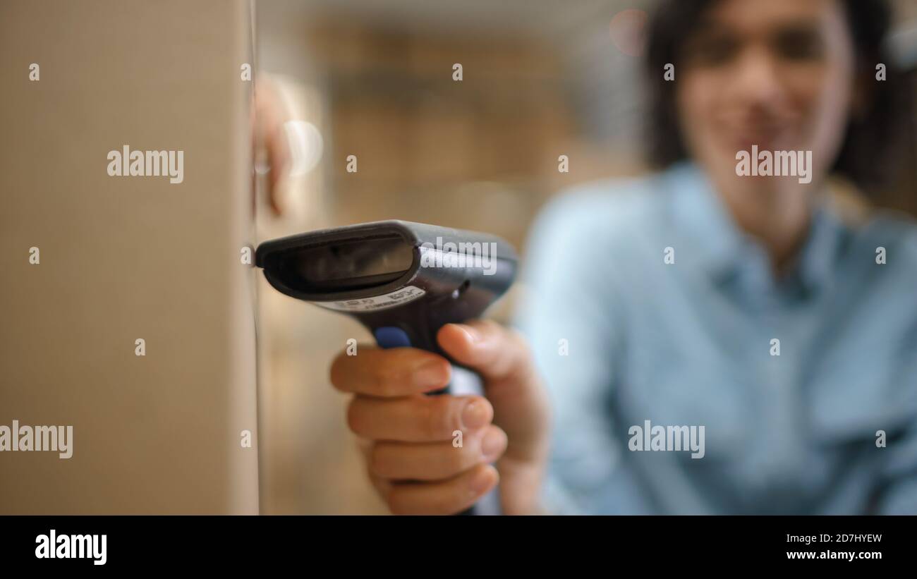 Close-up Shot of Female Inventory Manager Scans Cardboard Box and with Barcode Scanner. In the Background Rows of Cardboard Boxes with Products Ready Stock Photo