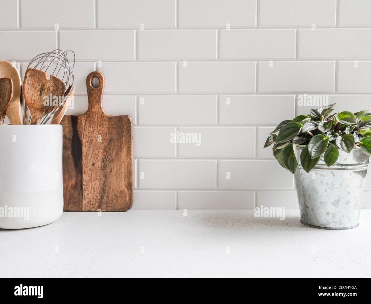 Stylish white kitchen background with kitchen utensils and green houseplant standing on white countertop, copy space for text, front view Stock Photo