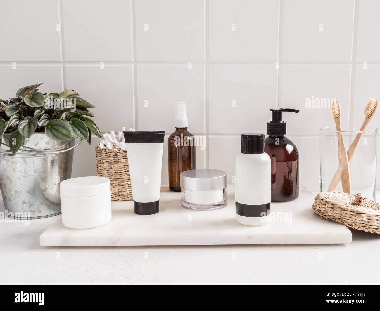Stylish white bath background with cosmetic bottles, bath accessories and greenhouse plant on white shelf and wall tiles, place for text, bathroom in Stock Photo