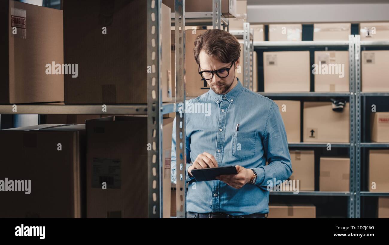 Warehouse Inventory Manager Uses Tablet Computer to Check Stock on Shelves. Rows Of Shelves with Cardboard Box Parcels full of Products Ready for Stock Photo